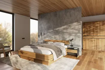 Holzbett mit heller Decke und hellen Kissen freistehend vor einer Betonwand im hellen Schlafzimmer.