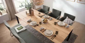 Großer Massivholz Esstisch mit verlängerter Tischplatte und schwarzem Fußgestell gedeckt mit Teller und Stühlen und Sitzbank um den Tisch.