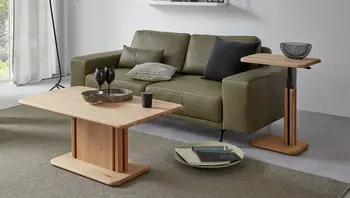 Couch- & Beistelltisch aus Holz vor einem grünen Ledersofa.