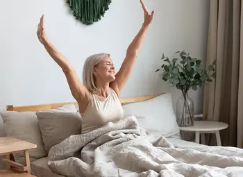 Natura Home Schlafzimmer mit Bett, Schrank in Holzoptik und Frau die sich streckt