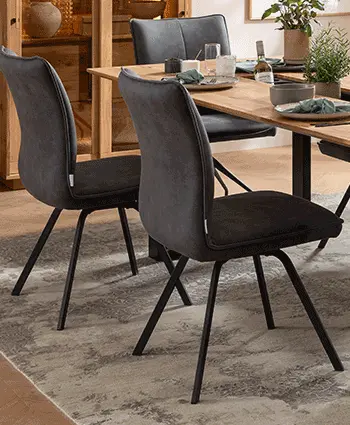 Zwei graue Esszimmerstühle mit schwarzem Gestell an einem Massivholz Esstisch.