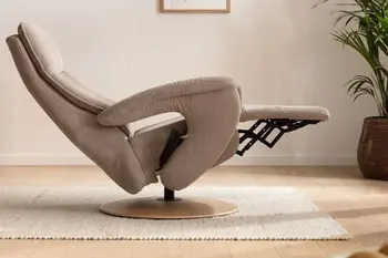 Seitliche Aufnahme eines beigen Relaxsessels, der sich in Liegeposition befindet in einem hellen Zimmer mit cremefarbenem Teppich und einer kleinen Palme.