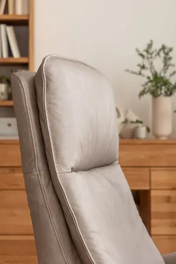 Bequem gepolsterte Kopflehne eines grauen Sessels mit Lederbezug.