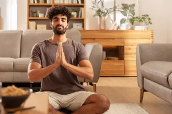 Ein Mann sitzt in Buddha Pose vor zwei grauen bequemen Ledersofas.