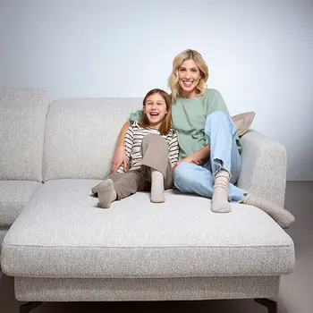 Mutter und Tochter sitzen lachend auf einem hellgrauen, modernen Sofa – harmonisches Familienmoment auf großzügiger Relaxfläche in gemütlicher Wohnumgebung.