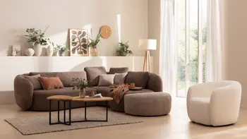 Gemütliches Wohnzimmer mit rundem braunen Sofa mit dazu passendem Hocker, Sessel und einem Couchtisch aus der gleichen Serie mit Massivholztischplatte und Metallgestell.