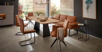 Moderner Esstisch aus Massivholz Eiche mit schwarzem Fußgestell, um den Stühle und eine Sitzbank mit Lederbezug in Cognac in einem modernen Esszimmer.
