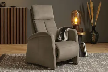 Grauer Relaxsessel mit hohen Armlehnen und hoher Rückenlehne in einem gemütlichen Raum mit Beistelltisch und Tischlampe und großer Vase mit Pampasgras.