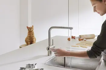 Frau steht an einer modernen Sensorarmatur einer Küche.