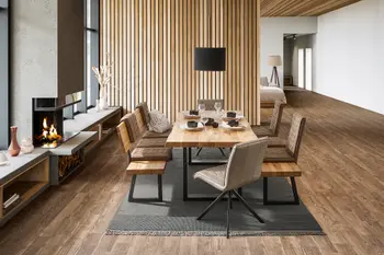 Esstisch mit Baumkante und Kufenfußgestell aus schwarzem Metall um den dazu passende Sitzbänke mit Rückenlehne und braunen Sitzpolstern stehen.