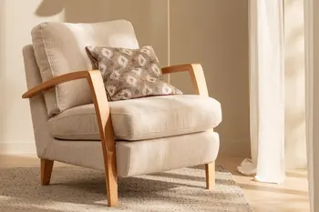 Sessel mit Armlehnen aus Holz und cremefarbenem Stoffbezug, auf der Sitzfläche liegt ein Kissen mit braune-beigem Muster.