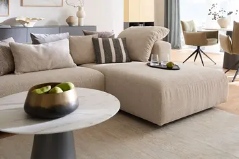 Detailbild von edel eingerichtetem, offenen Wohnzimmer mit beigem Ecksofa und rundem Beistelltisch in Marmoroptik.