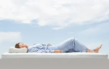 Eine Frau liegt auf einer Matratze unter blauem Himmel.