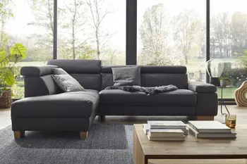 Blaugraues Ecksofa mit Kopfstützen und Holzfüßen vor einer großen Fensterwand.