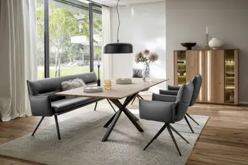 Moderne graue Armlehnstühle aus Leder mit schwarzem Fußgestell und eine graue Leder Sitzbank mit schwarzem Fußgestell um einen Massivholz Esstisch in einem hellen Raum.