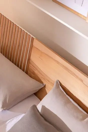 Ansicht von oben auf ein Bett, das ein Kopfteil aus hellem Holz hat mit Lamellenakzenten auf der linken Seite.