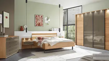 Helles Schlafzimmer mit Schlafzimmermöbeln. Ein Bett aus Holz mit Nachtschränken sowie eine Kommode und ein Kleiderschrank aus Holz mit braunen Glaselementen. 