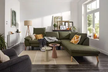 Grünes Ecksofa mit klappbaren Kopflehnen und hellen Holzfüßen, dekoriert mit mehreren Kissen und Decken in einem hellen gemütlichen Raum.