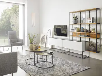 Helles Wohnzimmer mit Wohnwand mit vielen Regalen und weißem Sideboard vor einem grauen Sofa.&nbsp;