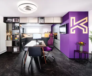 Grosse Musterkueche mit Beratungstisch neben lilafarbener Wand mit Kuechenhaus Gruber Logo.