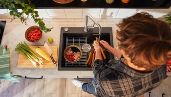 Junger Mann wäscht buntes Gemüse an einer modernen Küchenspüle mit schwarzem Becken und Edelstahlarmatur, umgeben von frischen Zutaten auf der Arbeitsfläche.