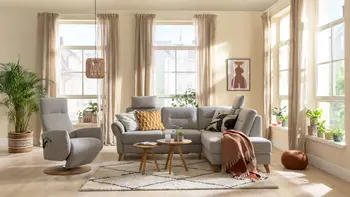 Graues Ecksofa mit bequem gepolsterten Rückenpolster und zwei Kopfstützen neben einem grauen Relaxsessel in einem gemütlichen Wohnzimmer.