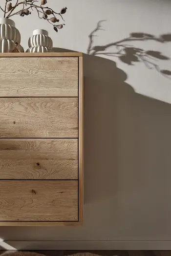Hängende Kommode einer Garderobe in hellem Holz, dekoriert mit weißen Vasen, in einer Vase sind Blumen.