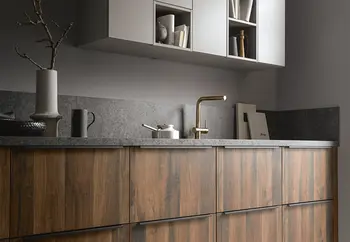 Küchenzeile mit Fronten aus dunklem Holz und grauer Arbeitsplatte mit einem goldenen Wasserhahn.&nbsp;