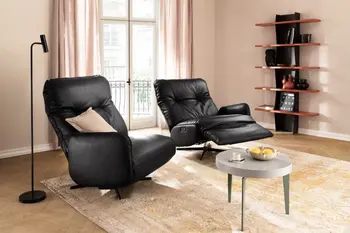 Zwei schwarze Ledersessel die nur auf jeweils einer Seite eine Armlehne haben, der rechte Sessel ist nach hinten gelehnt in Relaxposition.