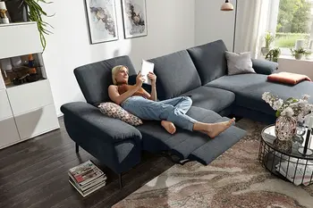 Frau entspannt auf grauem Sofa mit Relaxfunktion und liest ein Buch.