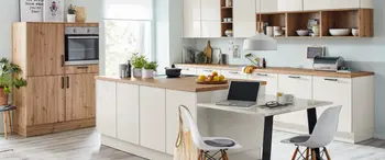 Puristische Küche mit weißen Fronten und Holzarbeitsplatte. In der Mitte eine Insel mit integriertem Essbereich mit Stühlen.&nbsp;