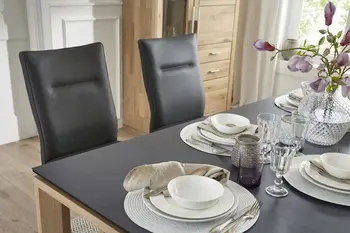 Gedeckter Esstisch mit schwarzer Tischplatte, an dem schwarze Lederstühle stehen.