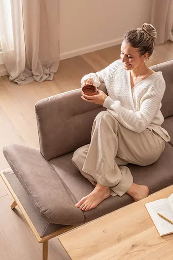 Frau sitzt entspannt mit einer Tasse Tee auf einer gemütlichen Esszimmerbank mit braunem Stoffbezug.