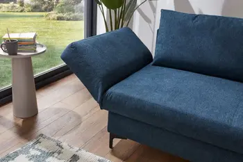 Petrolfarbenes Sofa mit leicht nach oben geklappter Armlehne in einem hellen Raum.