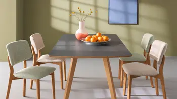 Esszimmer mit viel Lichteinfall und grüner Wand, sowieo einem grauen Esstisch und 4 verschiedenfarbigen Stühlen. 