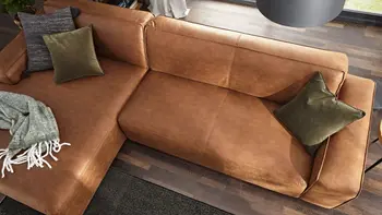 Cognacfarbenes Ecksofa von oben mit grünen Kissen und grüner Decke.