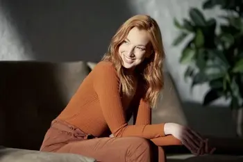 Eine Frau sitzt zufrieden lächelnd auf einem grauen Ledersofa.