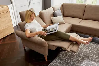 Frau sitzt gemütlich auf einem braunen Ledersofa, das eine Relaxfunktion hat.