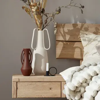 Nachttisch aus hellem Holz, der an Bett angebracht ist und mit Vasen dekoriert ist.
