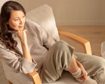 Frau sitzt entspannt mit Kopf auf der Hand gelehnt auf einem Stuhl und blickt in die Ferne.