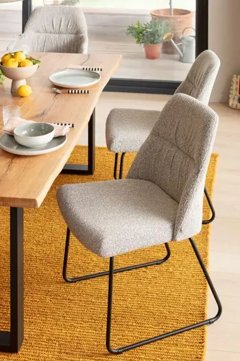 Grauer Esszimmerstuhl mit schwarzem Gestell an einem Massivholztisch.