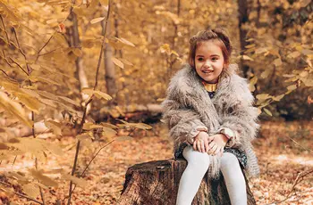 Kleines Mädchen sitzt im Wald auf einem gefällten Baumstamm.