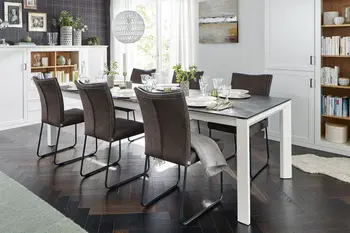 Großer Esstisch mit schwarzer Tischplatte und weißem Gestell, um den mehrere braune Lederstühle stehen.