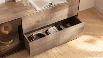 Dunkelbraunes Lowboard mit einer aufgeblätterten Zeitschrift und geöffneter unteren Schublade, mit Dekoelementen.