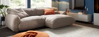 Graues Ecksofa mit bequemer gemütlicher Polsterung in einem hellen Raum mit zwei Hocker.
