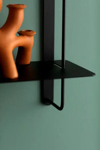 Moderne Deko in der Farbe Terrakotta auf einem schwarzen Wandregal an grüner Wand.
