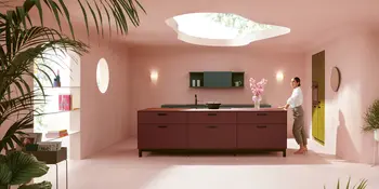 Frau in weinroter Design-Inselkueche mit gruenem Haengeschrank in rosa gestrichener Küche.