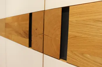 Detailansicht einer modernen Möbeloberfläche mit weißem Korpus und vertieft eingesetzten Massivholz-Elementen in Naturholzoptik.