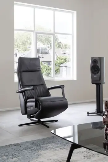 Schwarzer Relaxsessel mit Lederbezug und schwarzen Armlehnen und Fußgestell vor einem großen Fenster.