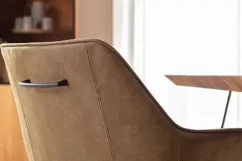 Seitenansicht eines Esszimmerstuhls in beige, der einen schwarzen Metallgriff an der Rückenlehne hat.